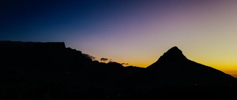 Lion's Head silhouetted against a deep blue and gold dusk sky over Cape Town