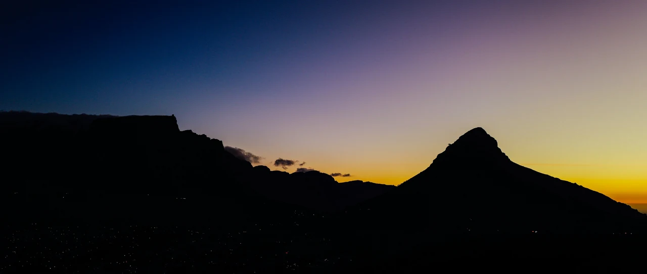 Lion's Head silhouetted against a deep blue and gold dusk sky over Cape Town