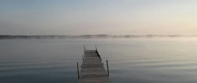 A wooden pier reaching into still, misty water at dawn