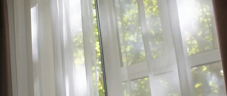 Sunlight through sheer white curtains at a window with green leaves outside