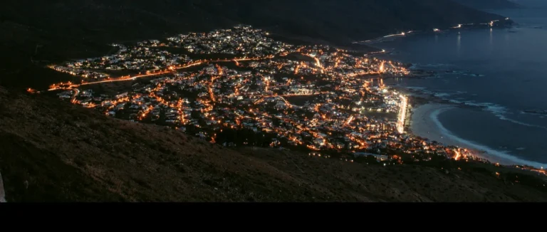 Camps Bay and the Atlantic seaboard lit up at dusk, seen from the mountainside above
