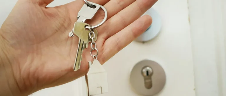 A hand holding house keys on a house-shaped keyring by a front door