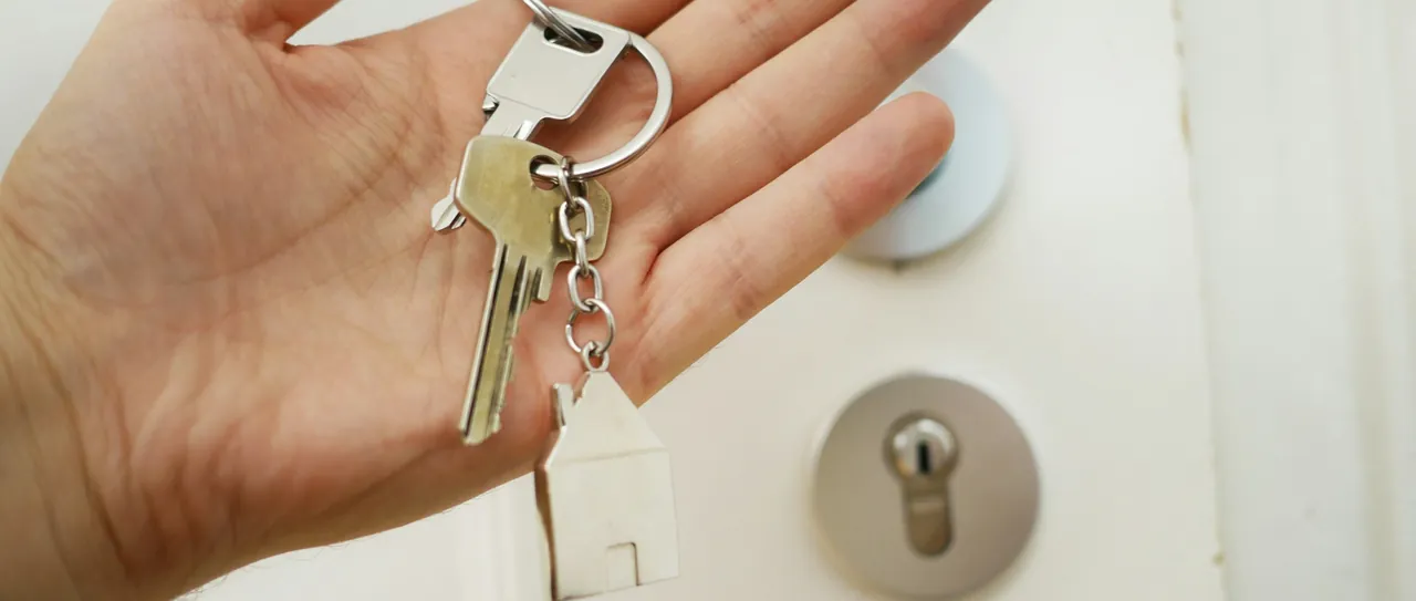 A hand holding house keys on a house-shaped keyring by a front door