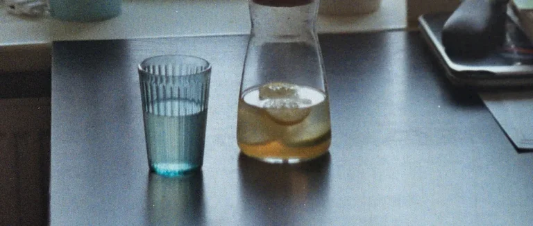 A glass and jug of water on a table by a sunlit window