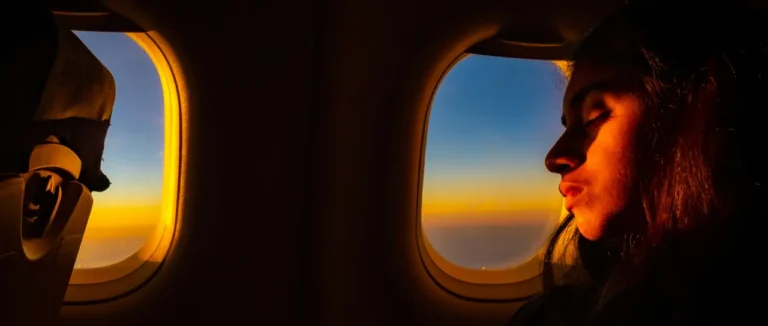 A passenger watching the sunset through an aircraft window on a long evening flight
