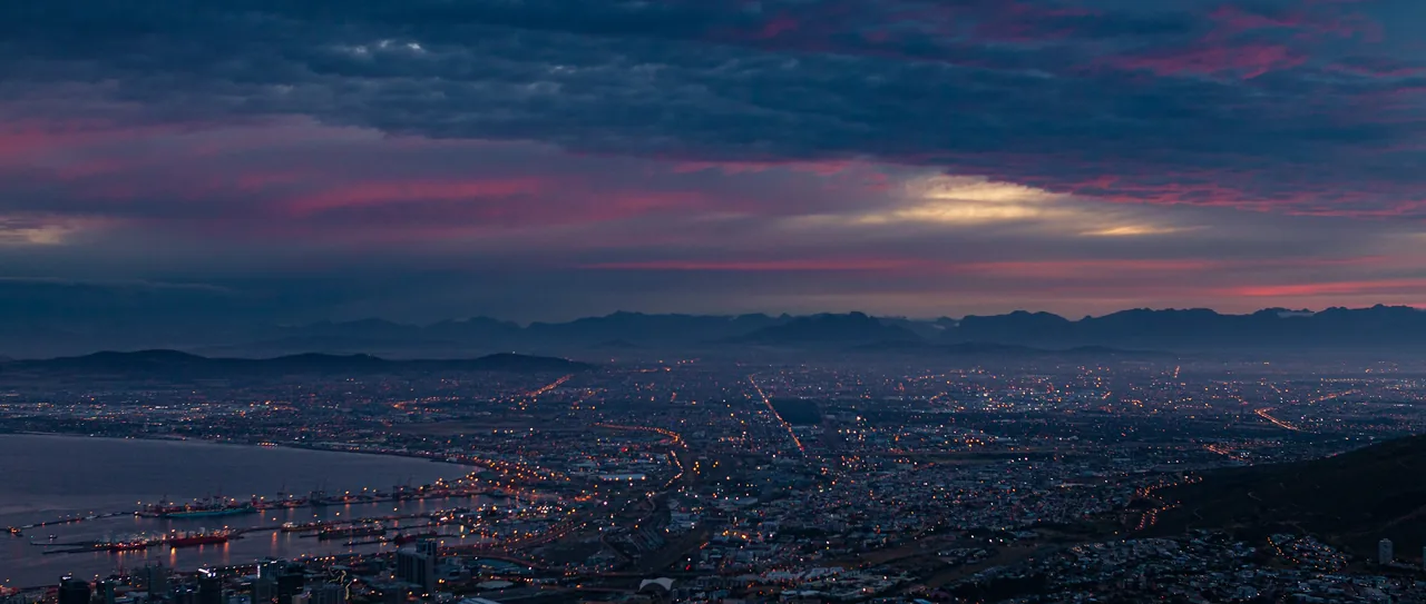 Aerial view of Cape Town city lights at dusk under a dramatic pink and blue cloudy sky