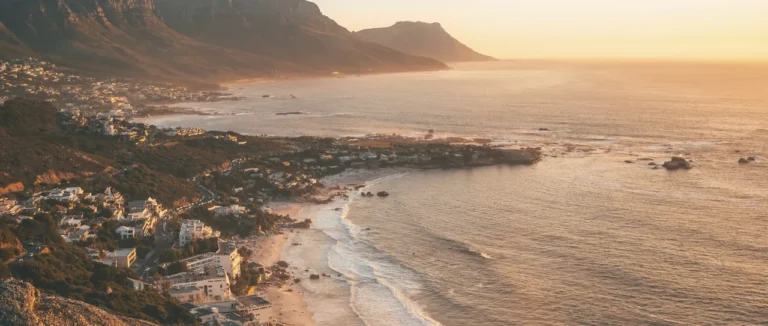 The Atlantic seaboard coastline at sunrise, mountains along the shore and a golden granite boulder in the foreground, Cape Town