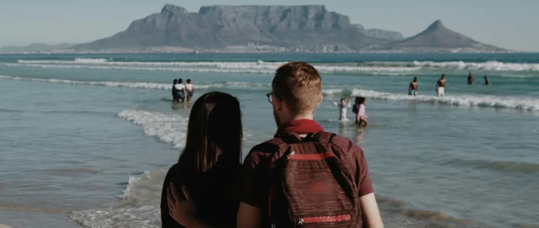 A couple on a Cape Town beach looking across the water at Table Mountain on a clear day