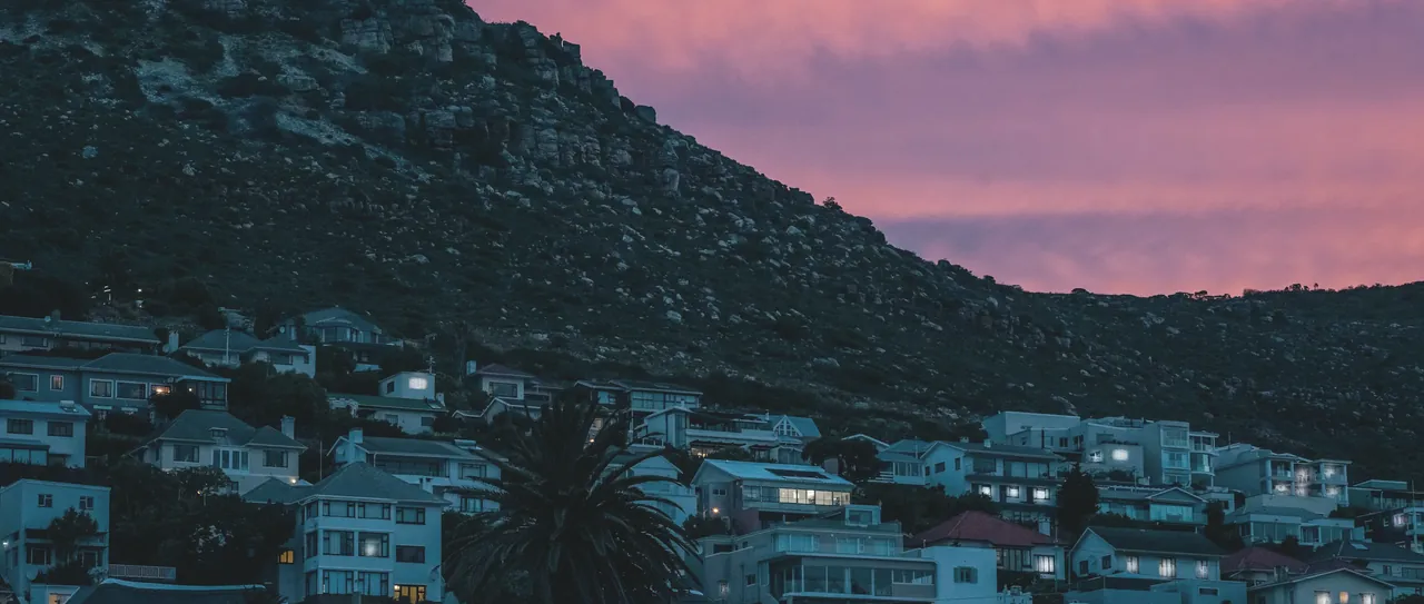 A hillside of houses above Fish Hoek lighting up at dusk under a pink evening sky