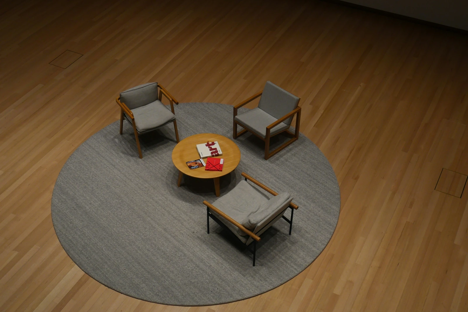 Three armchairs and a small round table on a round grey rug in an empty meeting room, seen from above