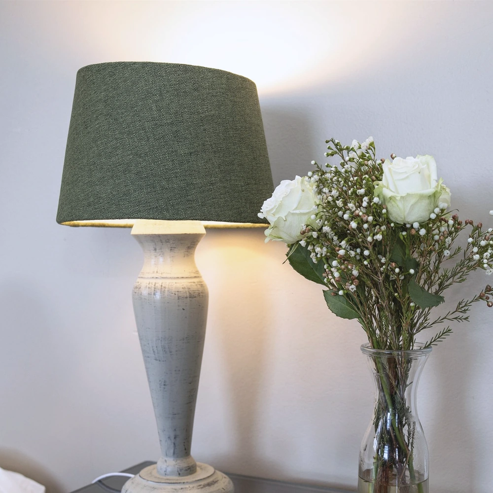 A lit bedside lamp beside a small glass vase of white roses against a pale wall