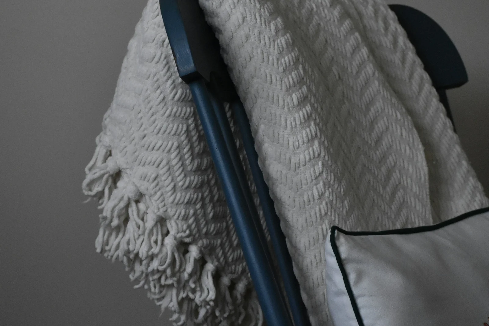 A soft grey blanket draped over the back of a chair in quiet, even light