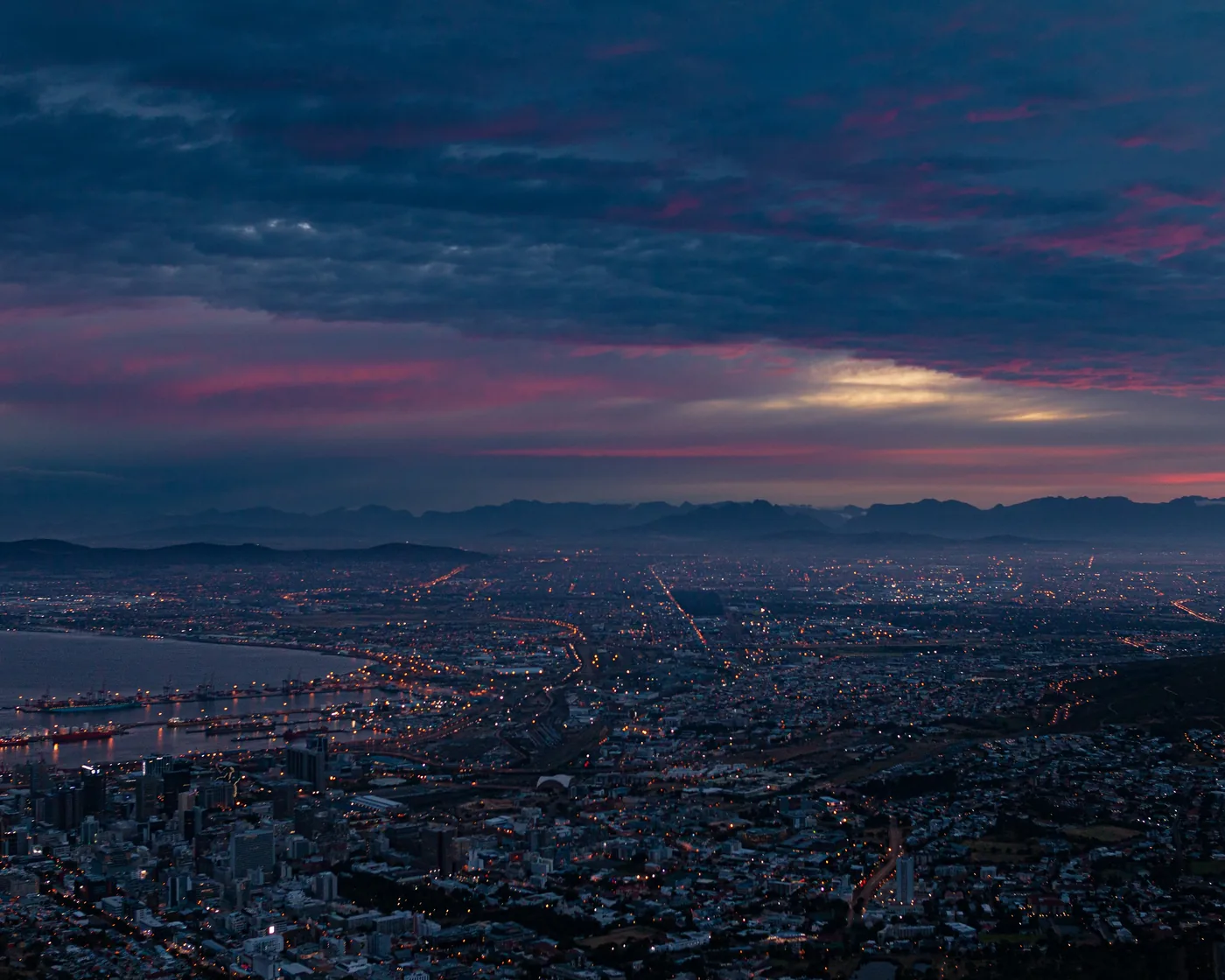 Aerial view of Cape Town city lights at dusk under a dramatic pink and blue cloudy sky