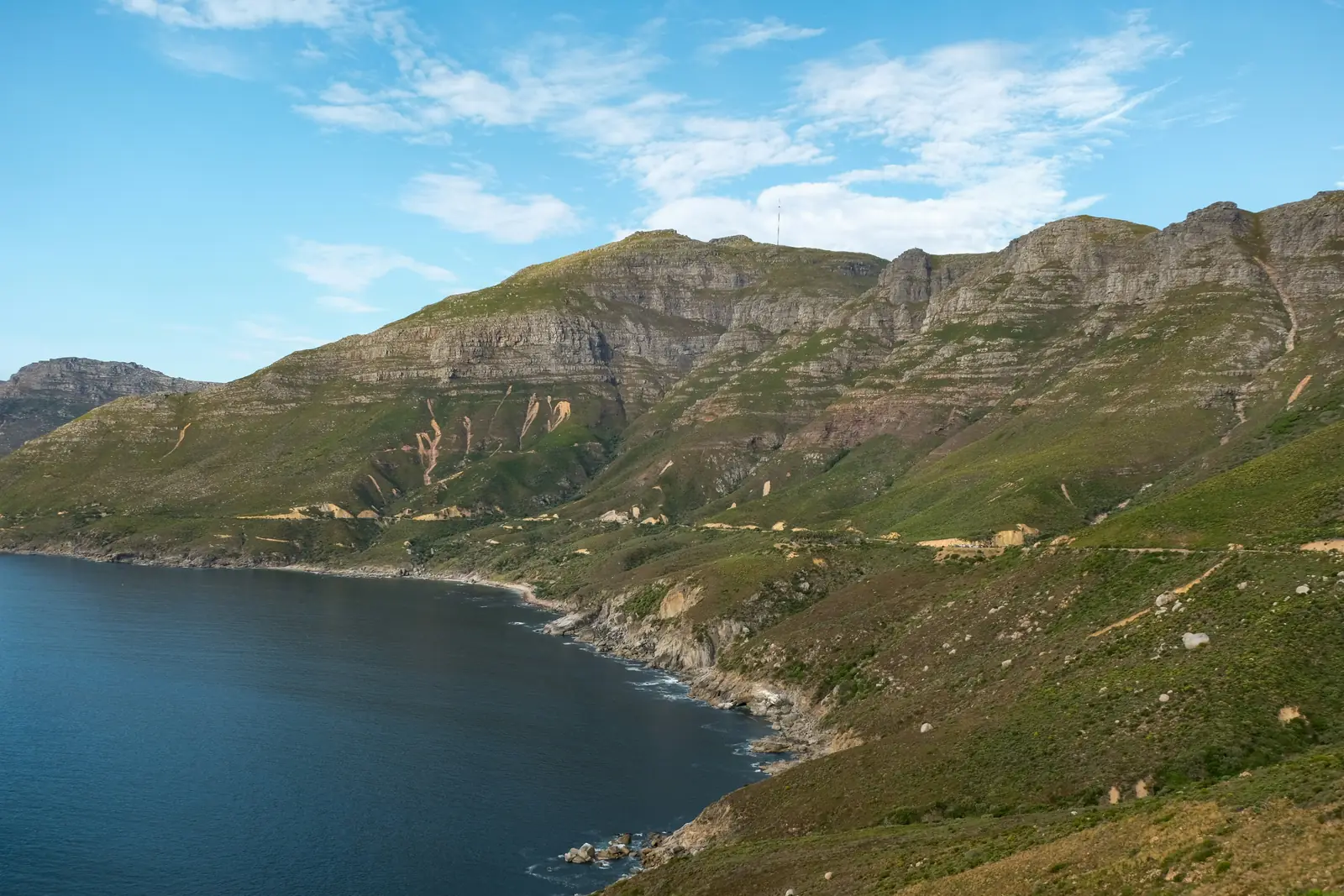 The coast road on Chapman's Peak Drive in Cape Town, cut into green mountains above the dark blue sea