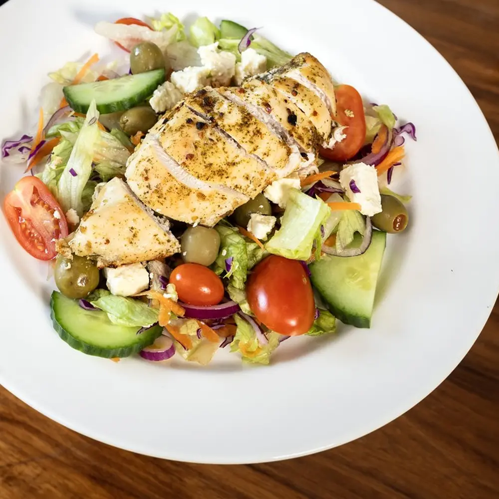 A plated Greek-style chicken salad with olives, feta and cherry tomatoes on a wooden table