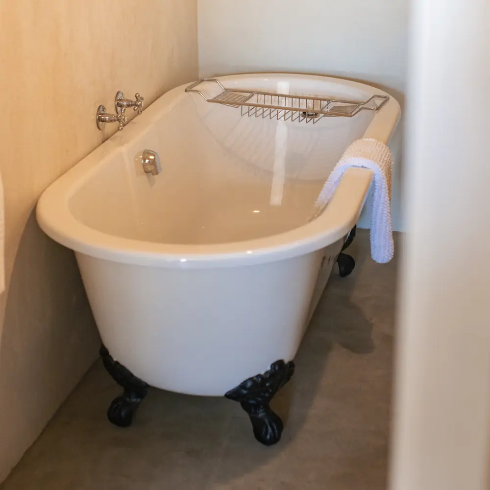 A white clawfoot bath with a wooden bath tray and a rolled towel in a quiet bathroom