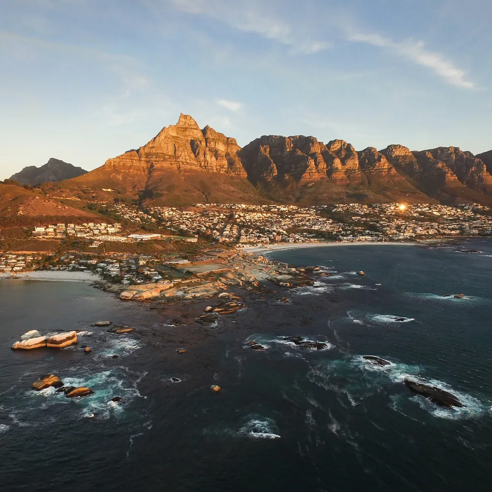 Camps Bay and the Twelve Apostles mountains above a calm bay, seen from the air in warm light