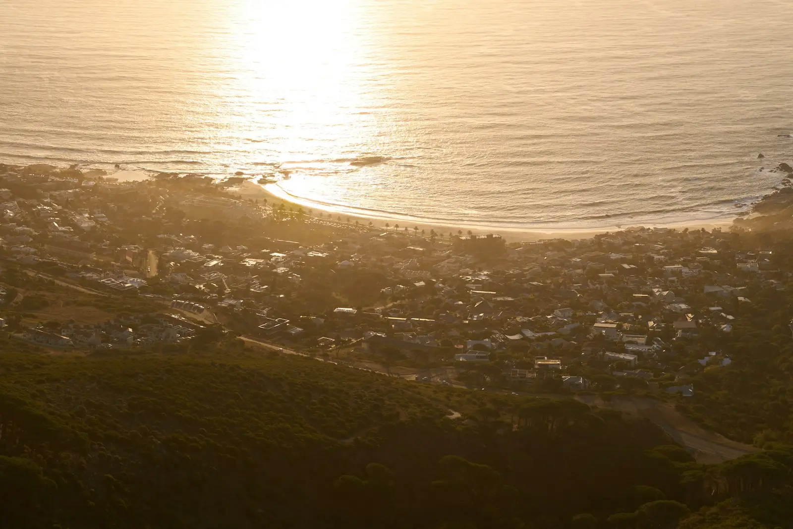 A coastal town glowing in low golden sunlight, seen from a mountain above the beach