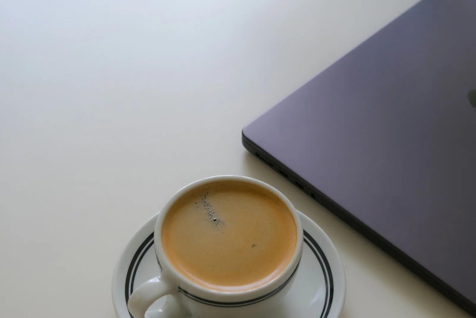 A closed laptop beside a cup of coffee on a plain desk