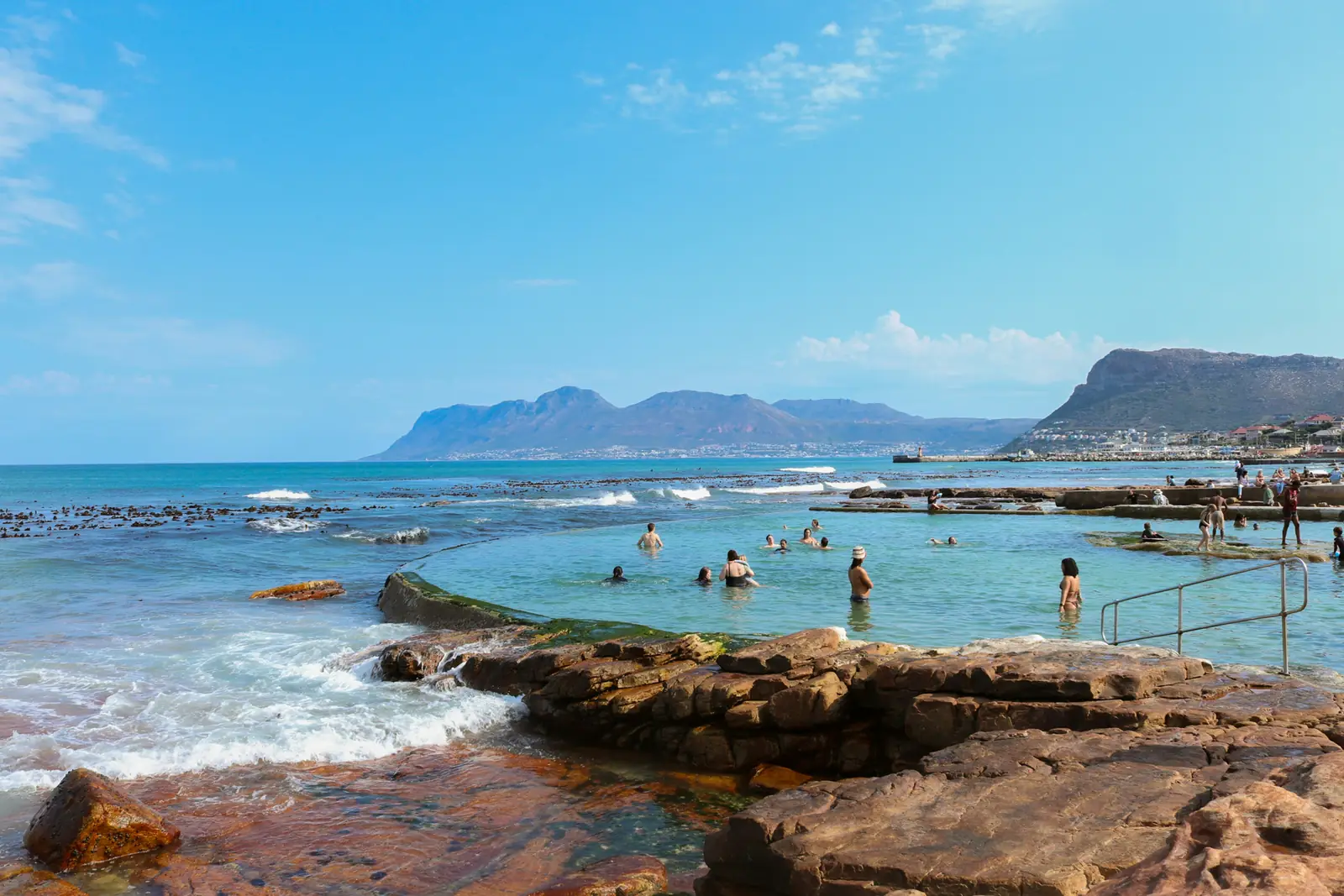 Swimmers in the Dalebrook tidal pool on the False Bay coast in Cape Town, with mountains across the water