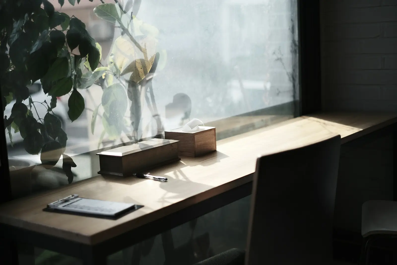 A tidy desk by a window, with a clipboard, a pen and a tissue box