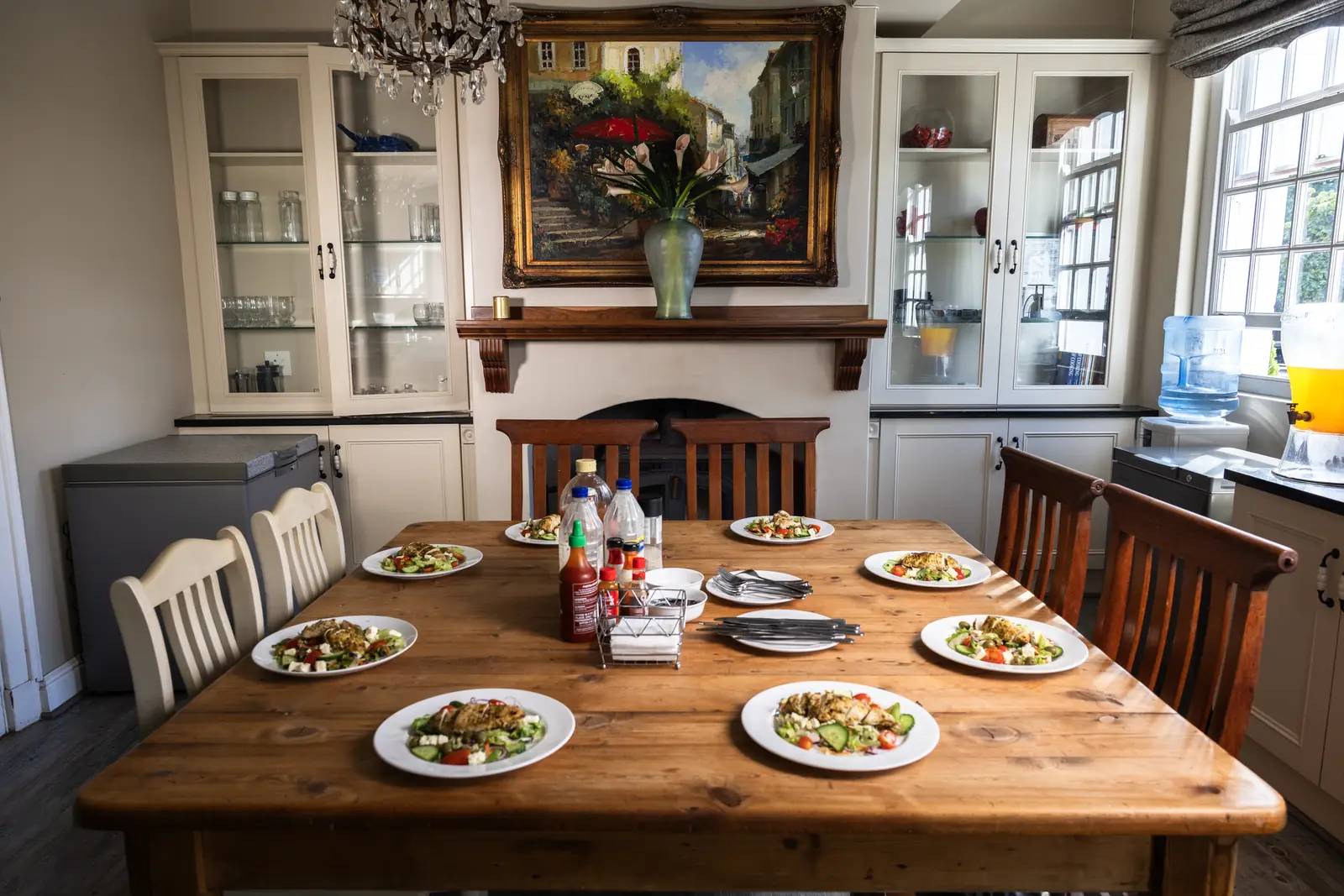 A wooden dining table set with plates of chicken salad in a dining room with a fireplace and an oil painting