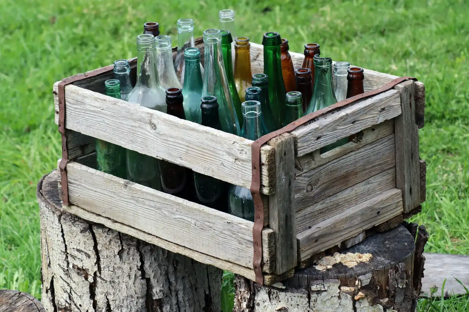 A weathered wooden crate full of empty glass bottles on a tree stump in the grass