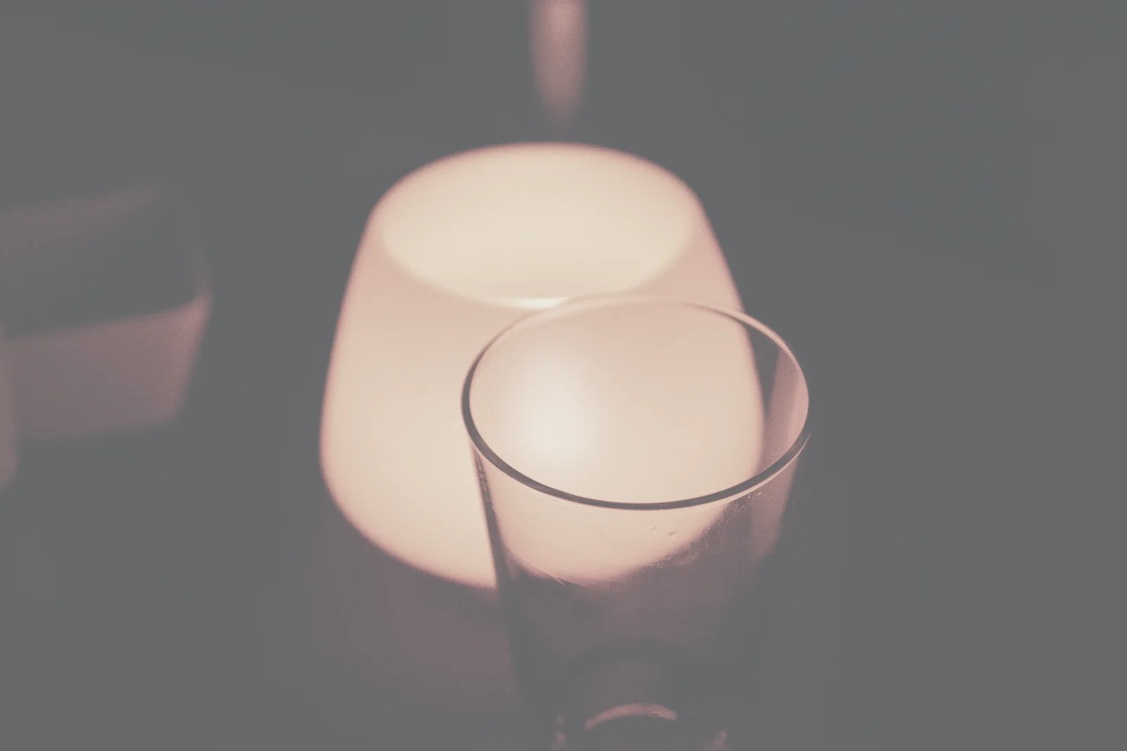 An empty drinking glass beside a glowing lamp on a table at night