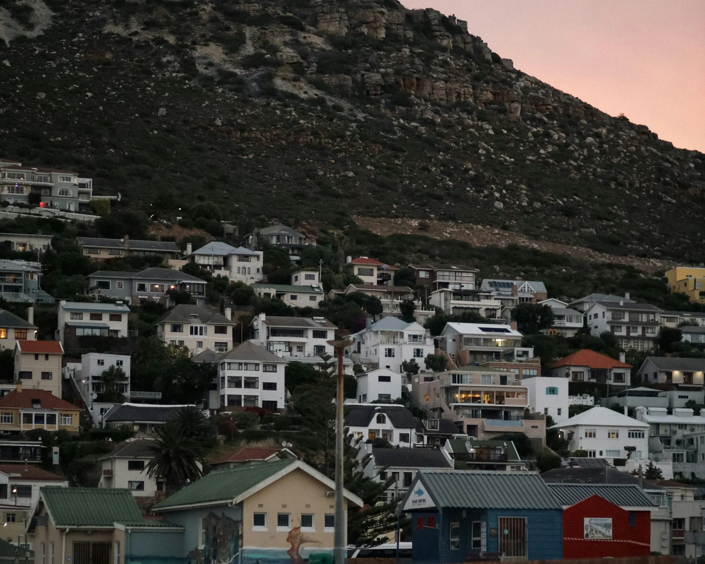 Whitewashed houses on a hillside at Fish Hoek at dusk with a pink evening sky above the mountain