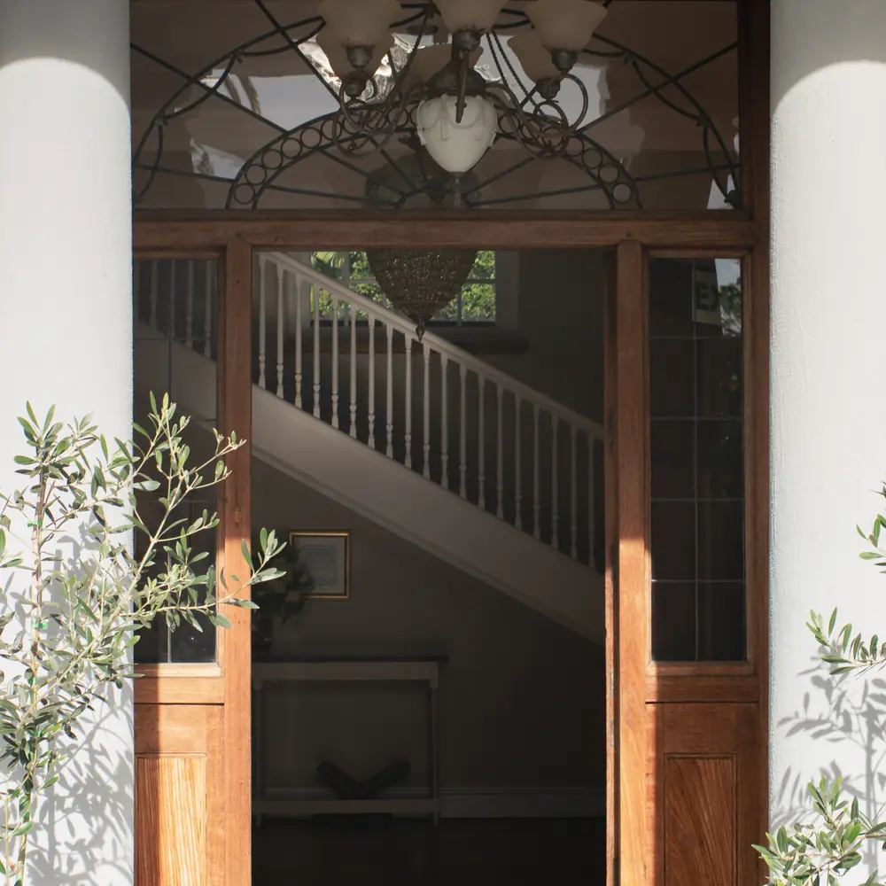 Open wooden front doors of the centre with a stained glass fanlight and a staircase in the hall behind