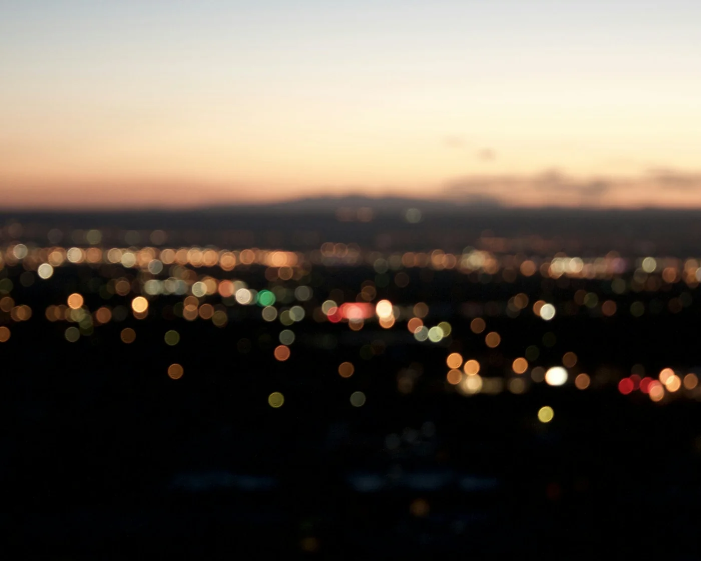 Defocused city lights at dusk with a faint mountain silhouette on the horizon