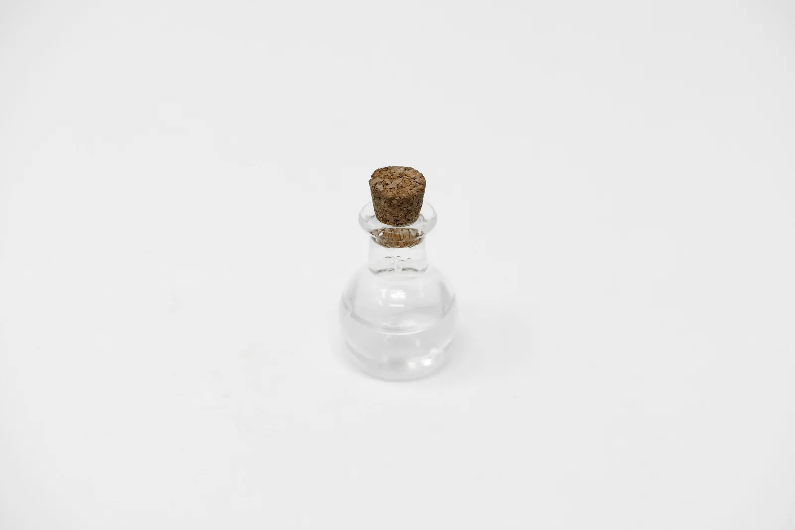 A small clear glass bottle with a cork stopper on a plain white surface