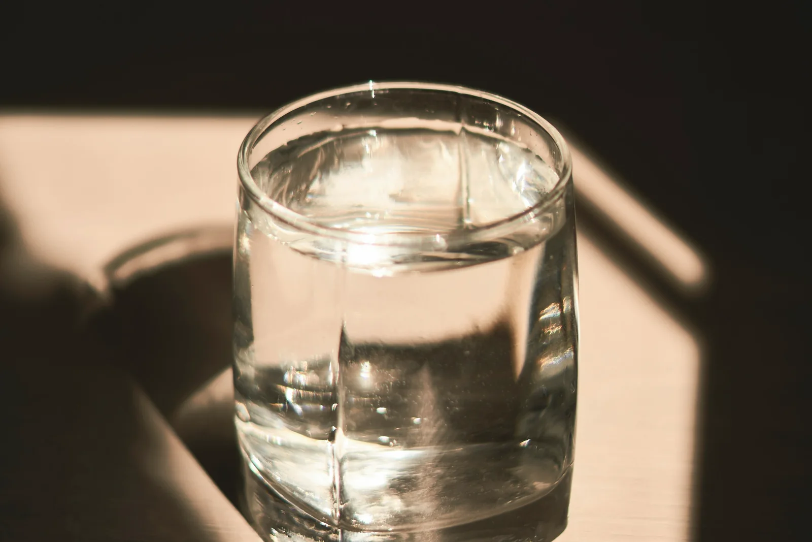 A glass of water catching warm lamplight on a bedside table at night