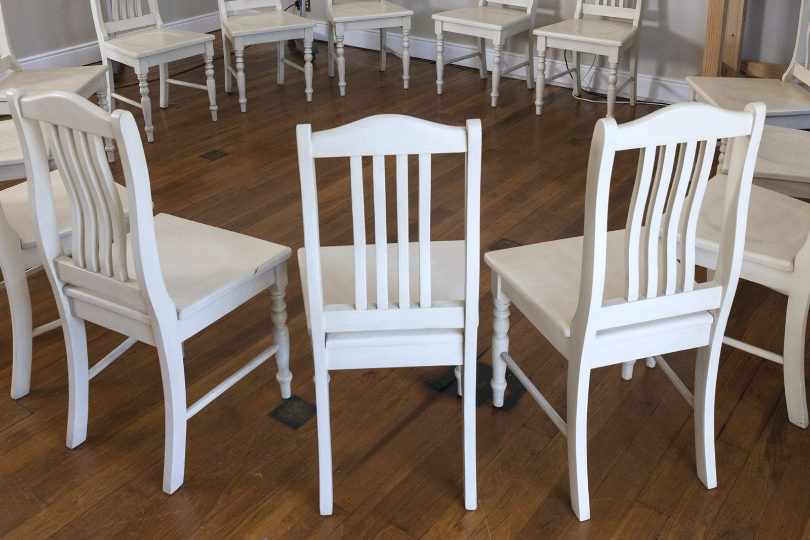 A circle of pale wooden chairs on a dark timber floor in an empty group therapy room
