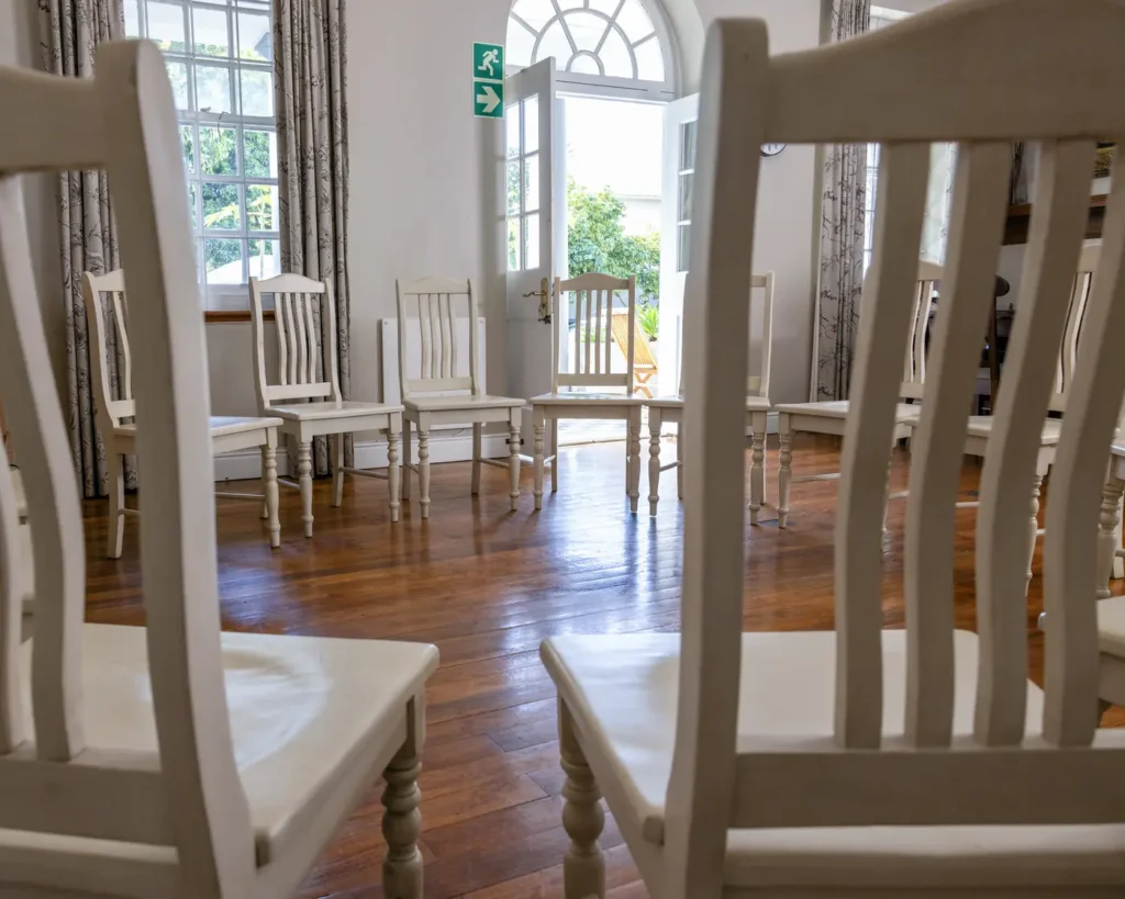 White wooden chairs set in a circle in a bright group therapy room, with French doors open to a sunny garden