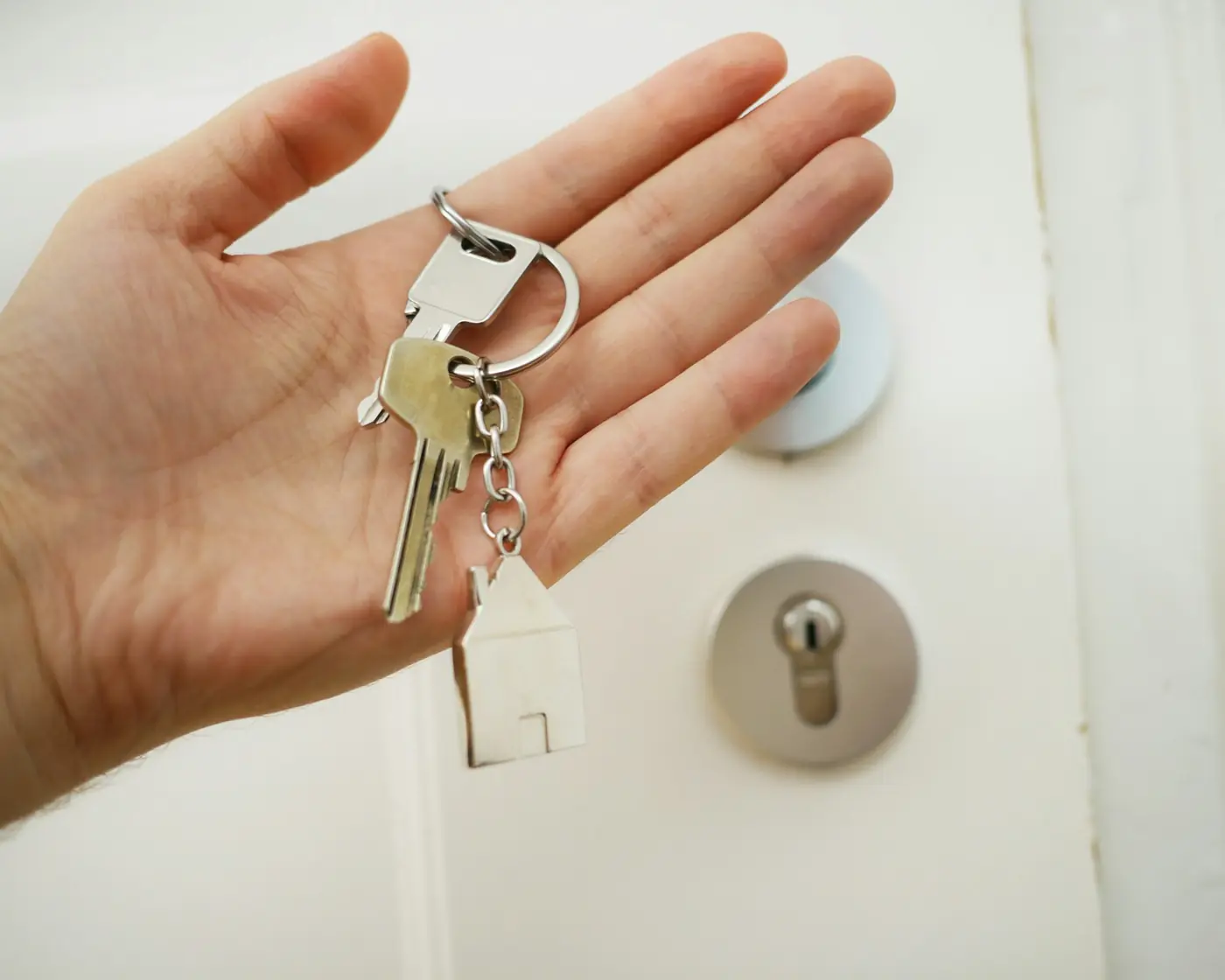 Open hand holding house keys on a house-shaped keyring by a front door
