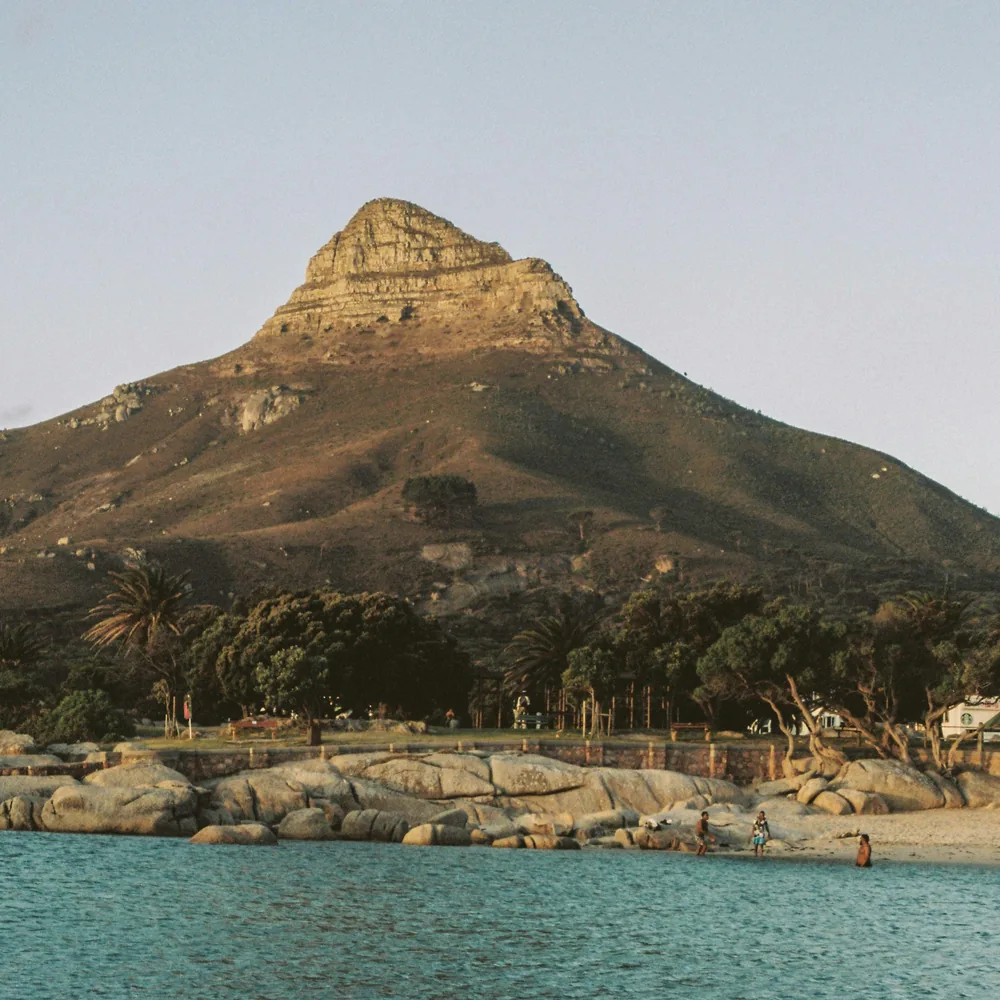 Lion's Head lit gold at low sun over a calm turquoise bay, trees and rocks along the shore below