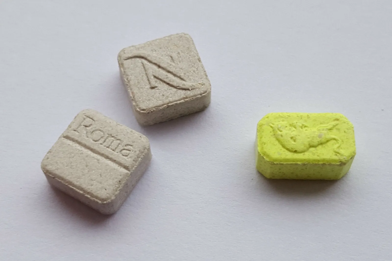 Three ecstasy tablets with stamped designs on a plain white surface