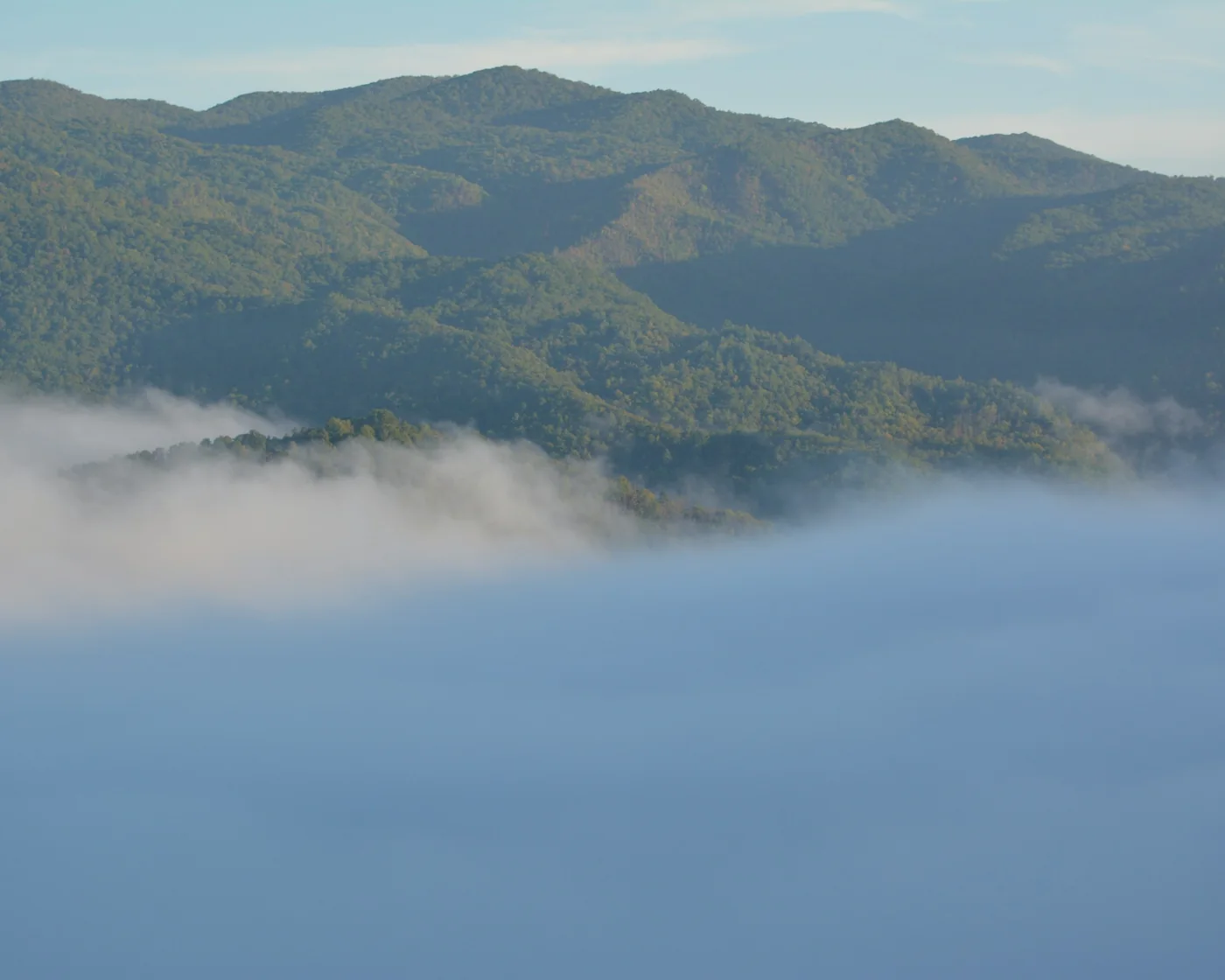 Misty mountain ridges rising above a blanket of morning fog under a clear sky