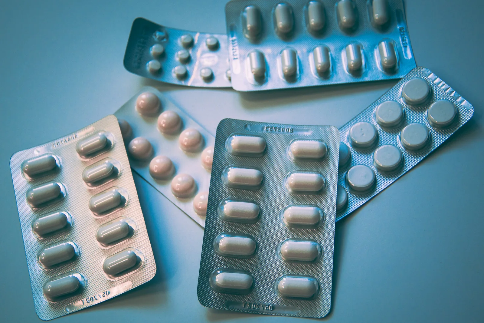 Several loose blister packs of white and pale tablets and capsules on a blue surface, no legible labels
