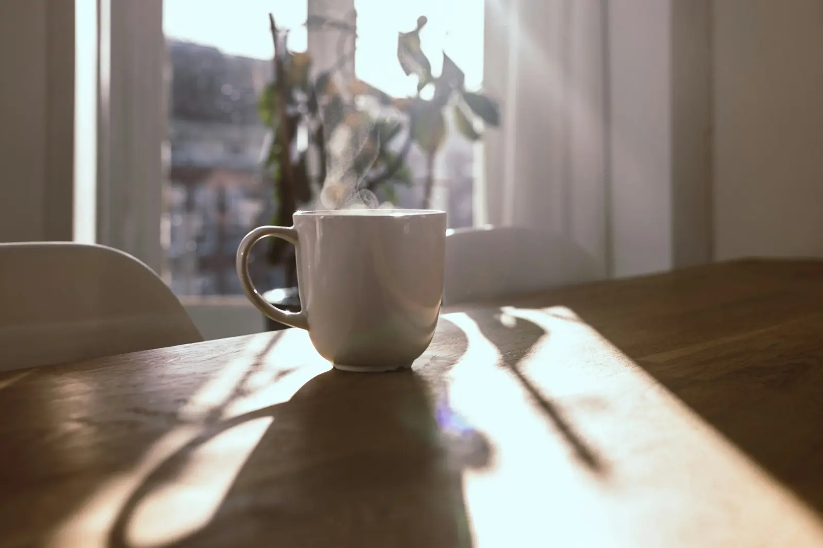 A steaming mug of coffee on a wooden table by a sunlit window