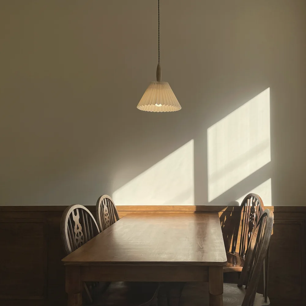 An empty wooden table and chairs lit by a shaft of morning sunlight, with a pendant lamp above