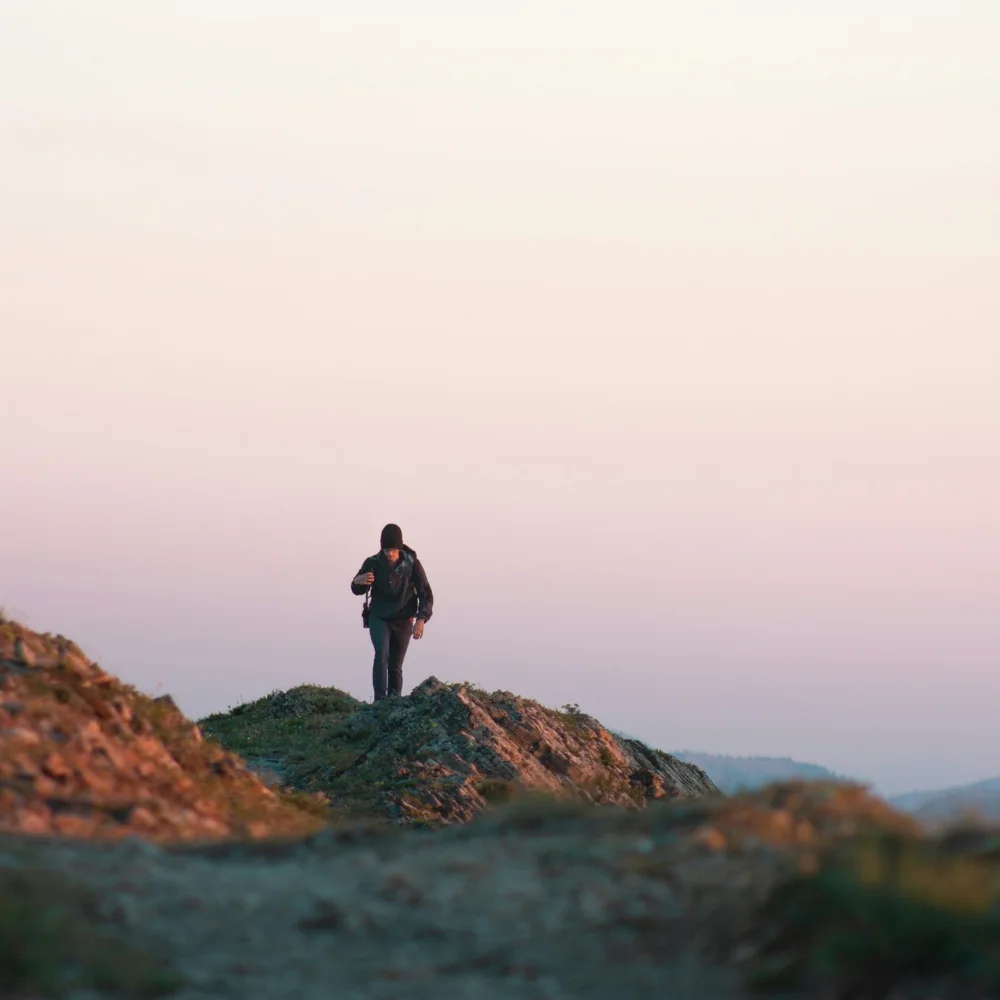 A hiker silhouetted on a ridge, climbing toward a pink sunrise over distant hills