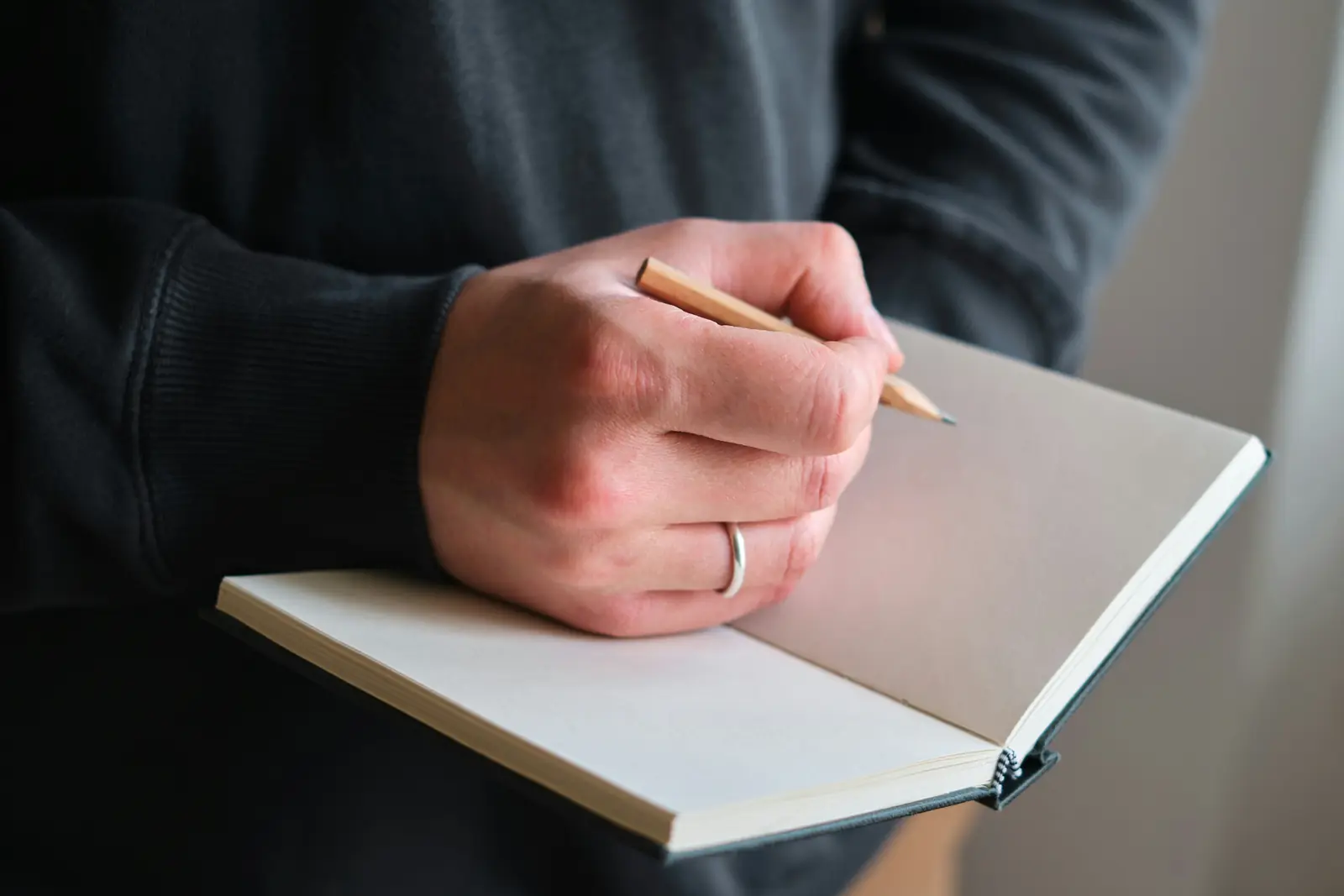 A person holding an open blank notebook and a pencil, ready to write down what they are told