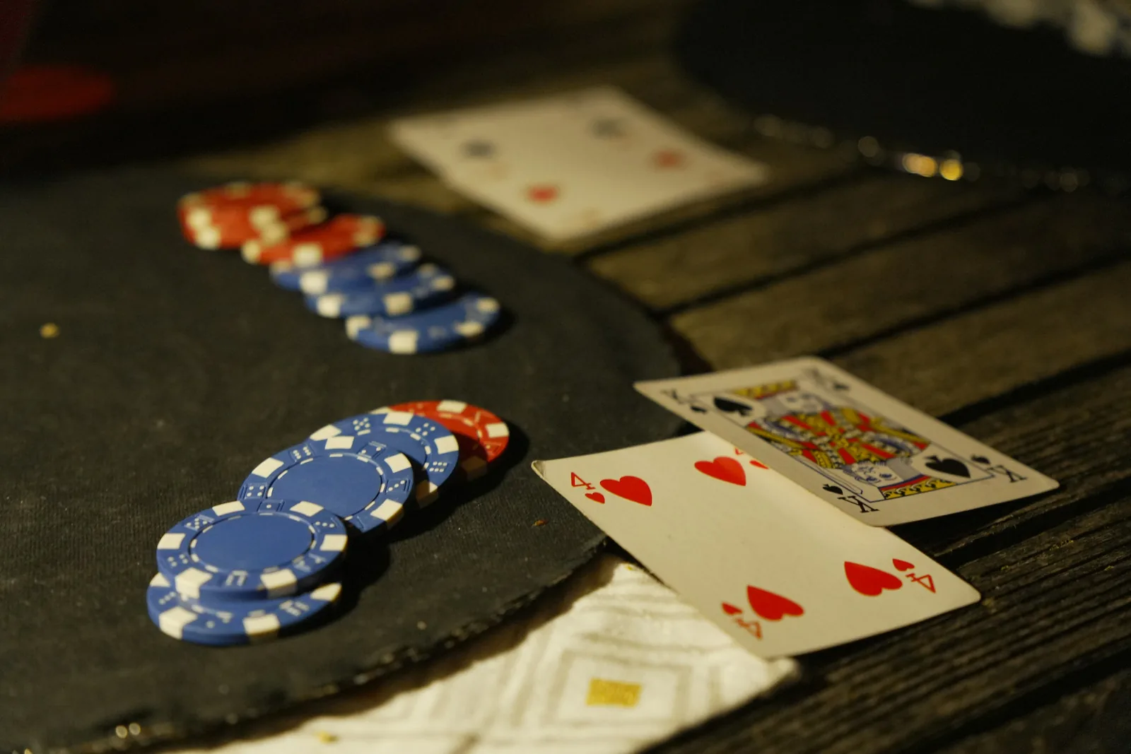 Poker chips and playing cards on a dark wooden table, lit by a single warm light
