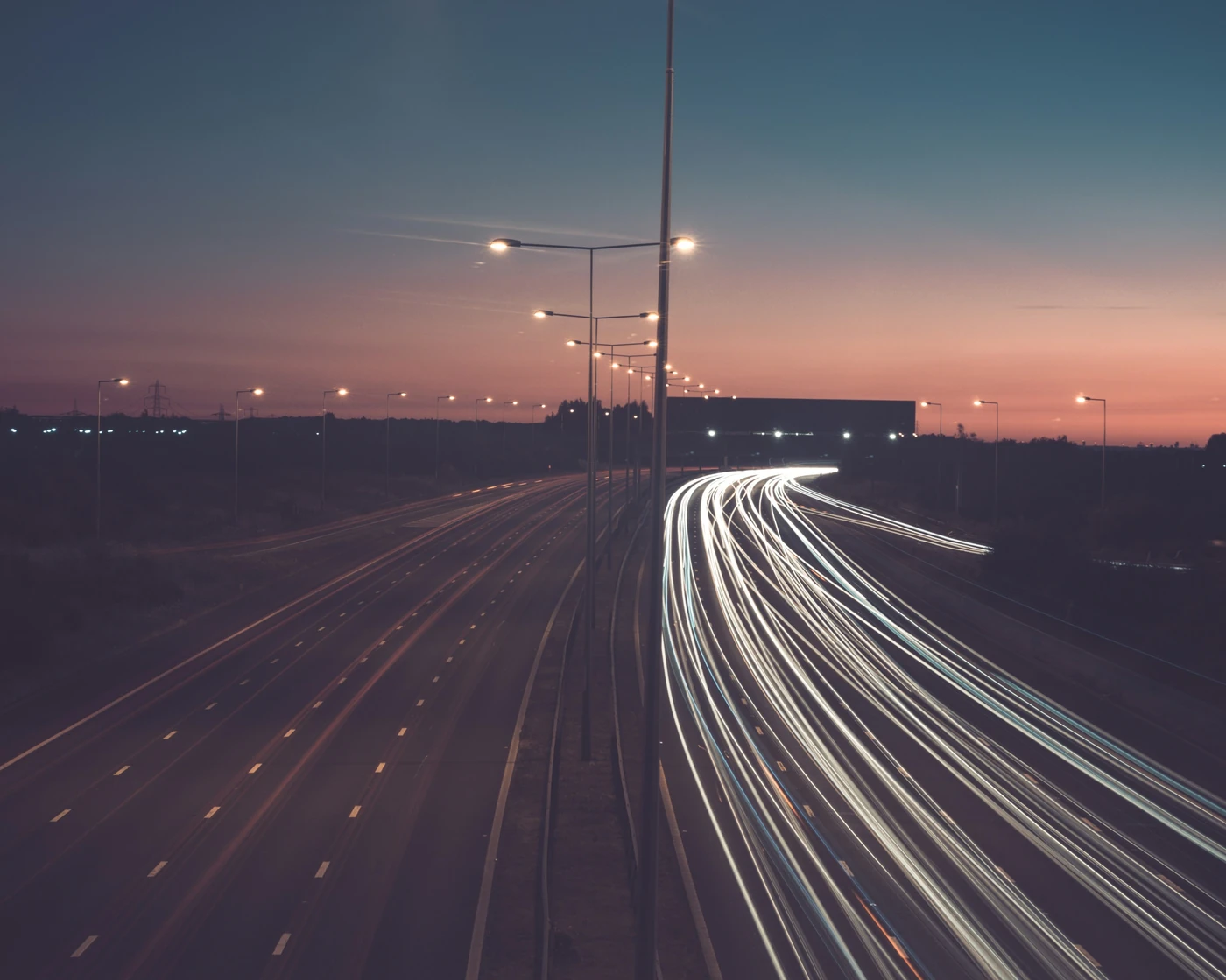 Streaks of white car headlights on an empty multi-lane road under street lamps at dusk