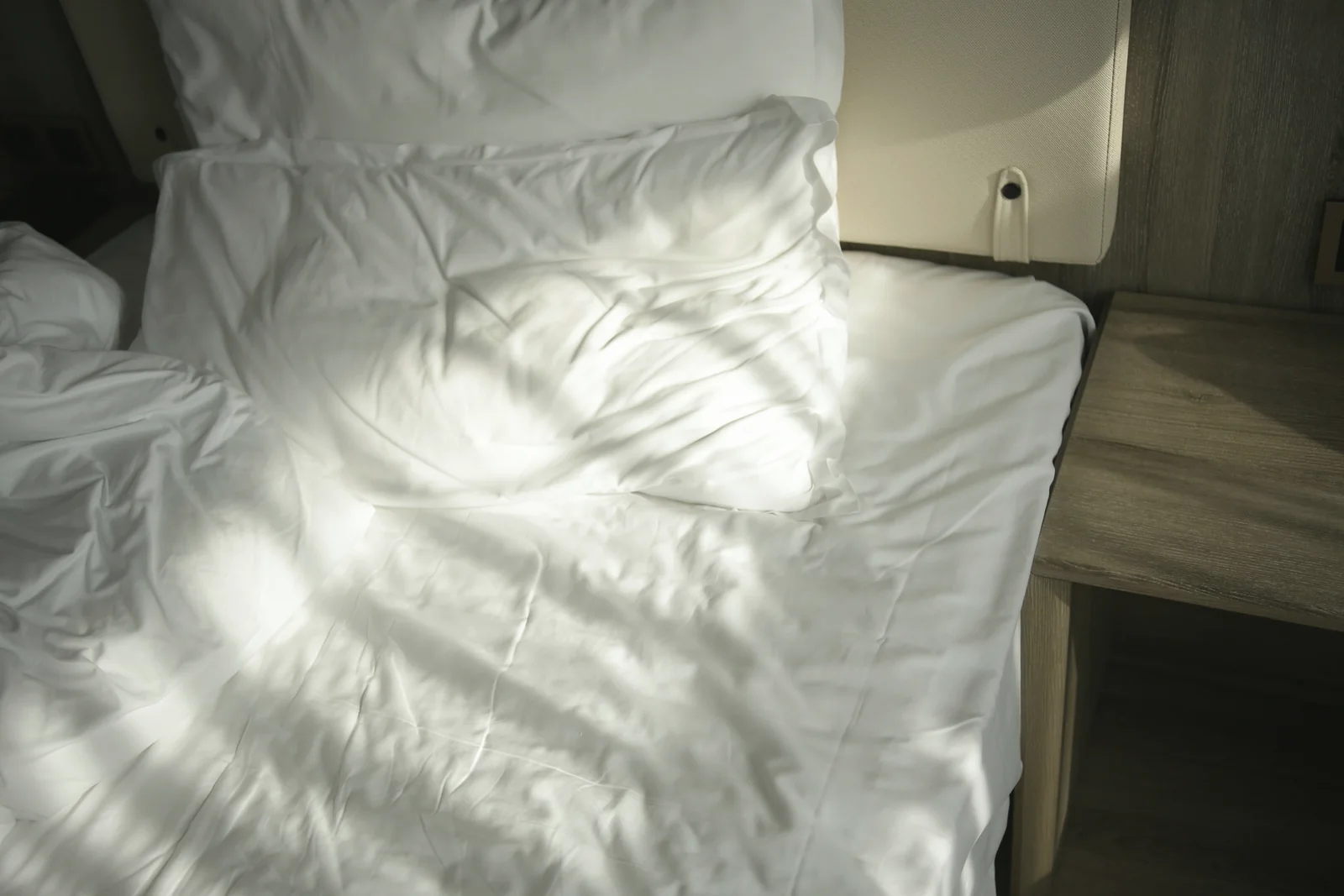 A rumpled, empty bed lit by morning sunlight coming through the window