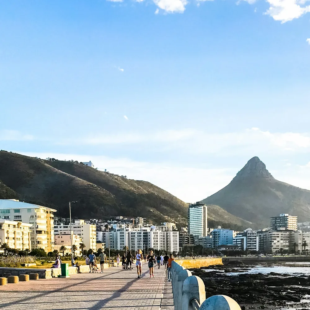 The Sea Point promenade in early morning light, Lion's Head ahead, the sea on the right and a few people walking