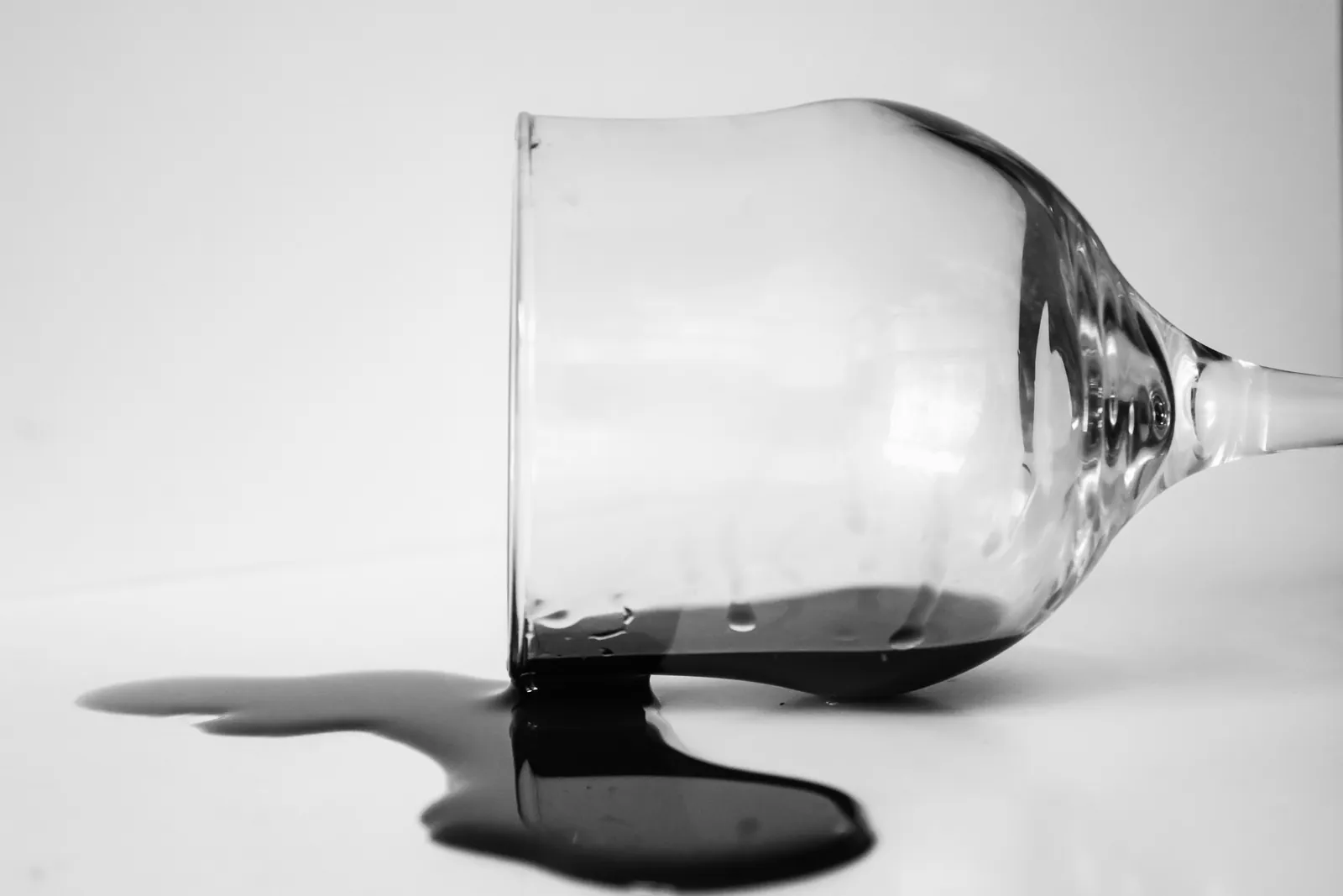 A tipped-over wine glass on a white table with spilled dark wine