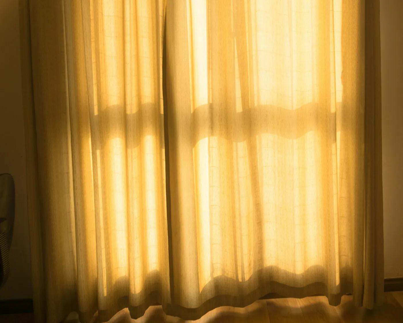 Warm evening sunlight glowing through cream linen curtains in a quiet room